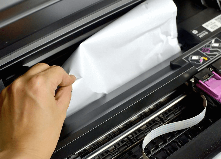 Someone's hand reaching to remove jammed paper from a jam in a printer/scanner