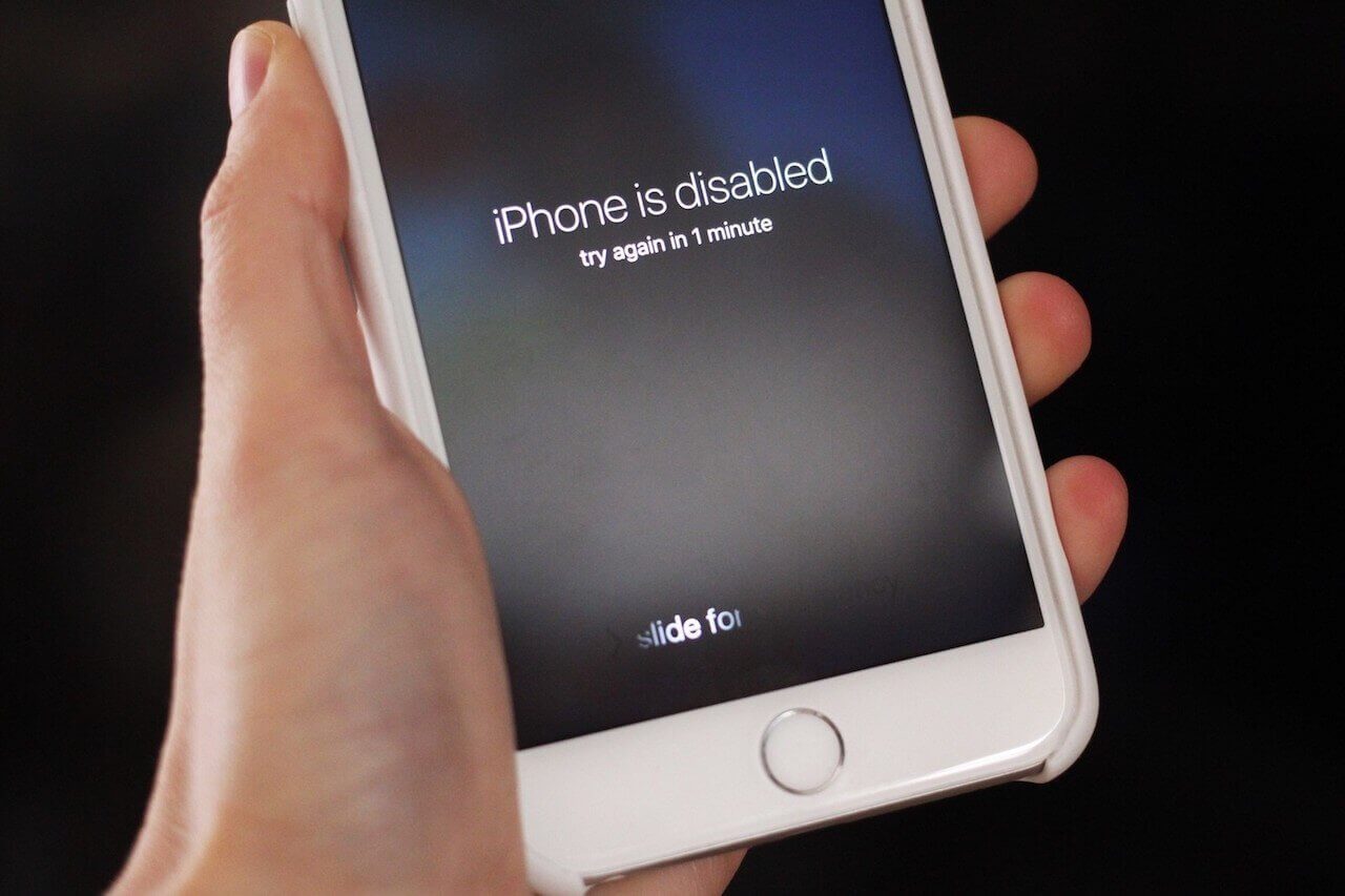 A hand holding an iPhone with the message, "iPhone is disabled".