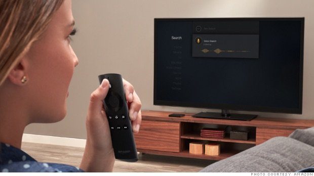 A blond haired woman holding a remote, pressing the voice control button, and giving a voice command to the TV in the background.